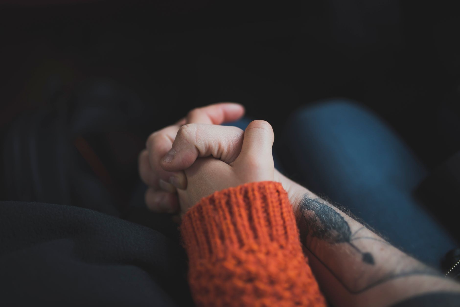 Close-up of two people's hands clasped together while seated on wooden chairs, one comforting the other.